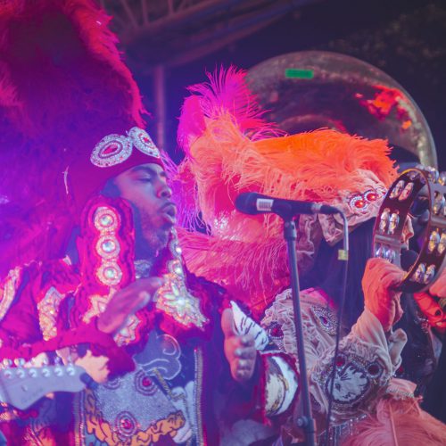 Musician in a vibrant, multi-coloured outfit, performing on stage in the evening