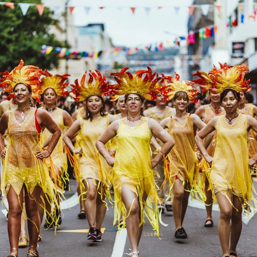 Batucada parade with women in yellow costumes, and yellow and red headdresses