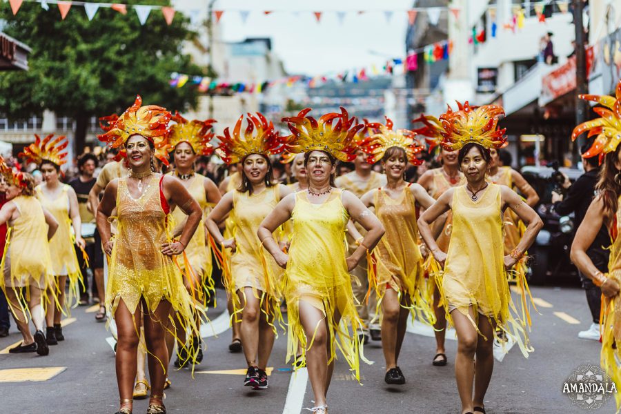 Batucada parade with women in yellow costumes, and yellow and red headdresses