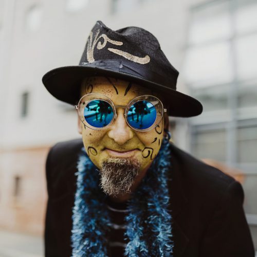 Close up of a street performer's face. He has yellow face paint and a black and blue costume
