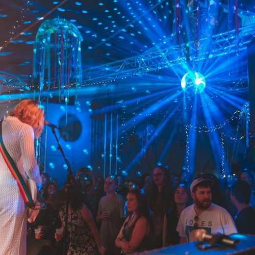Earth tongue performing in a white costume, with blue lights reflecting off a disco ball
