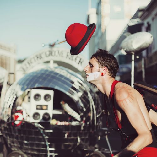 Street performer in black and red costume throwing and catching his red hat