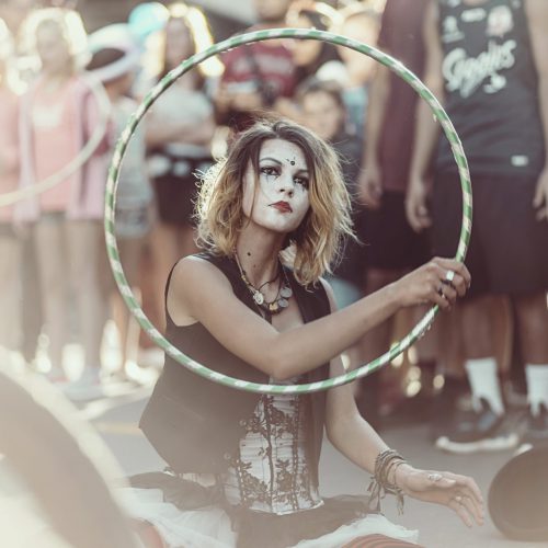 Street performer with white face paint sitting on the street doing an act with a hoola hoop