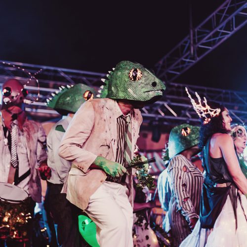 Batucada group performing in lizard costumes on stage at night