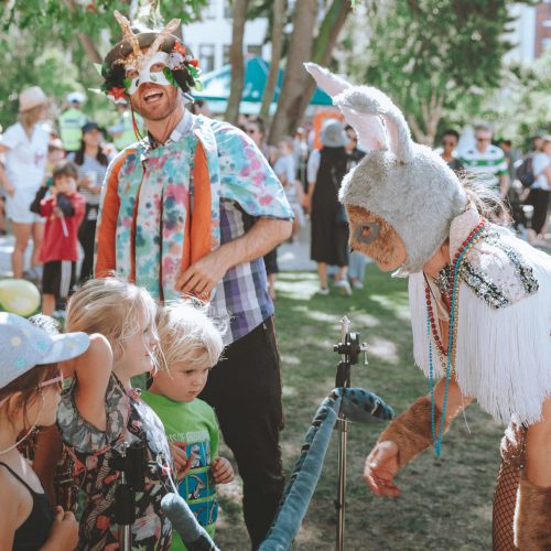 Two street performers in eclectic costumes interact with young children