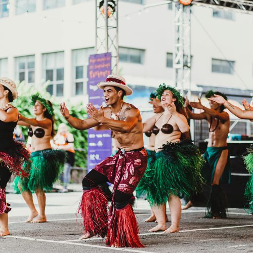 Men and women in grass skirts and pants doing a traditional Pasifika dance on the CubaDupa's Swan stage
