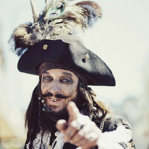 Close up of a man dressed as a pirate grinning and pointing at the camera