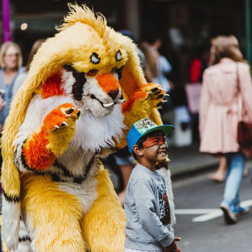 Adult in full body tiger costume standing behind a child with tiger face paint on