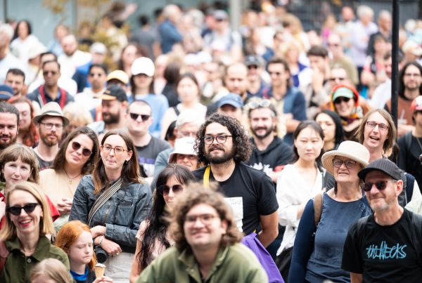 Smiling people in a crowd on Cuba Street, in the sunshine.